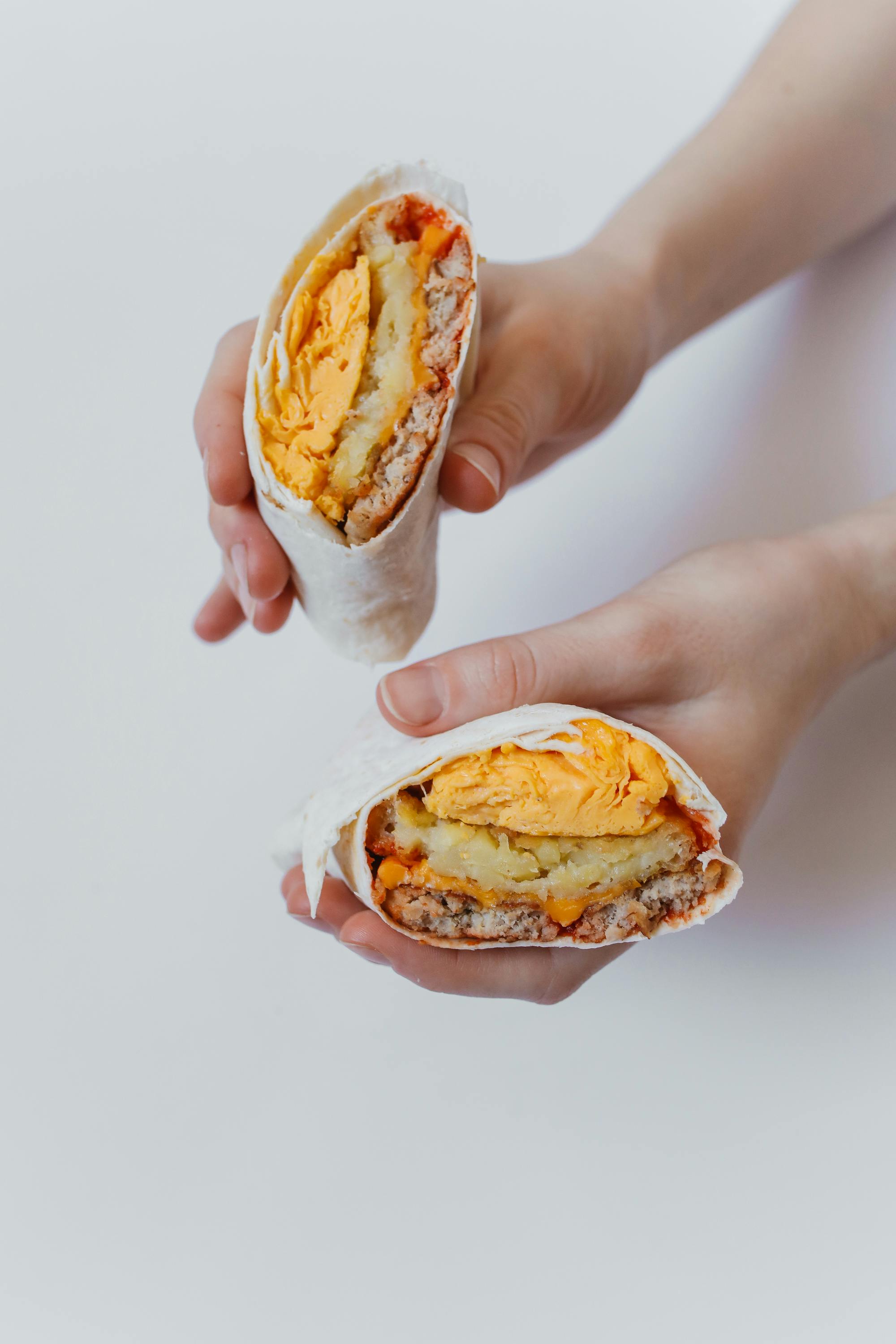 A breakfast burrito that has some hash-brown, eggs, sausage, and cheese