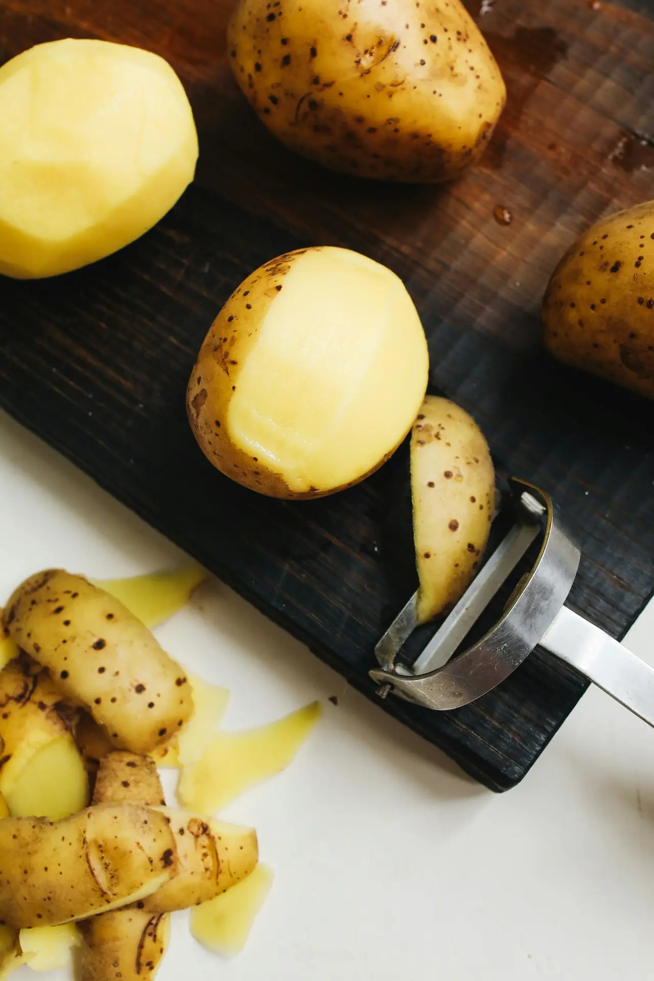 Potatoes on a cutting board, being peeled.